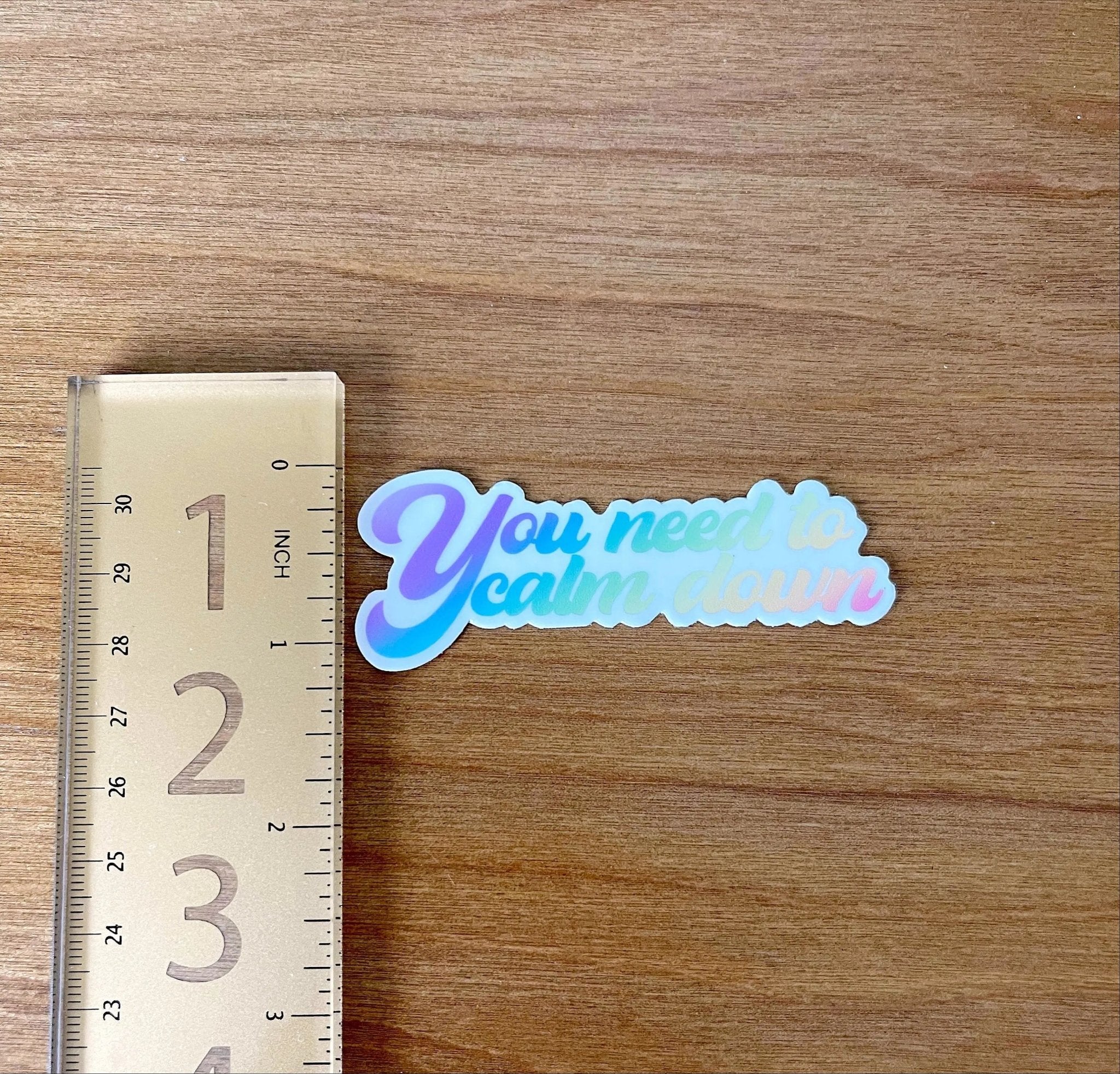 You need to calm down rainbow sticker flat lay — rainbow pride laptop sticker with hand lettered quote by indie artist MangoIllustrated