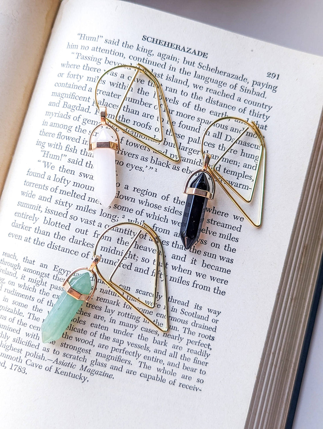 Three gold bookmarks with gemstone pendants on an open book