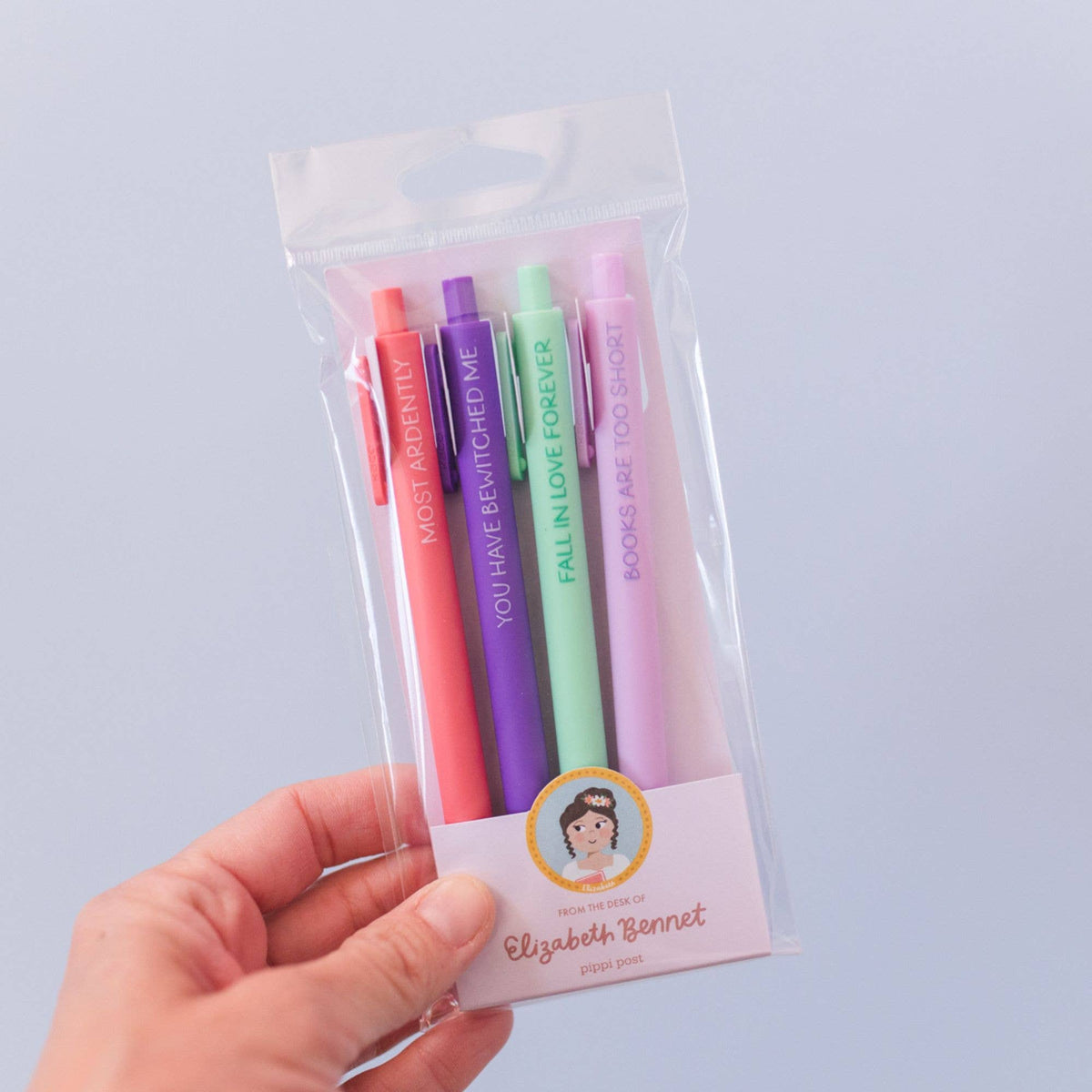 Set of colorful pens in a clear packaging with a hand holding it against a light purple background