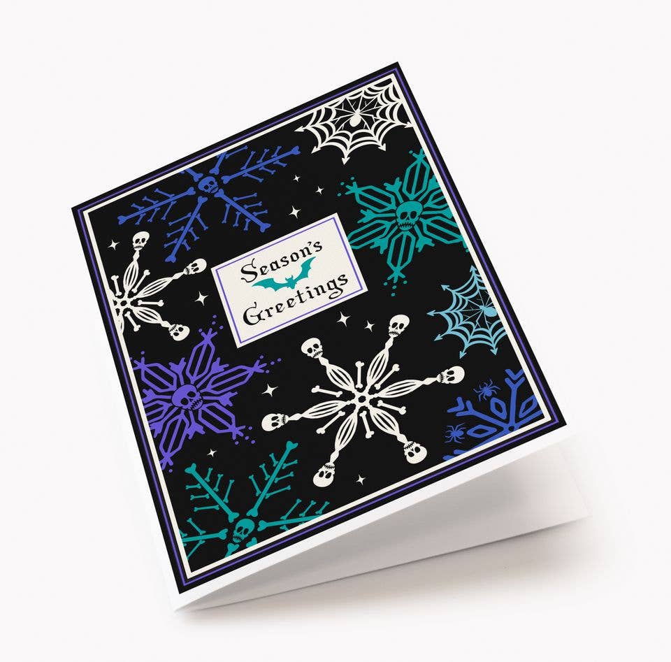 A square greeting card with a black background and seasonal winter motifs, including white snowflakes, purple and teal spiderwebs, and small white stars. A central white label reads &