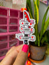 A hand with bright pink nail polish holds a die-cut sticker featuring a red-and-white knife with banners reading “LIVE,” “LAUGH,” and “LACERATE,” against a blurred pink organizer and green plant background.