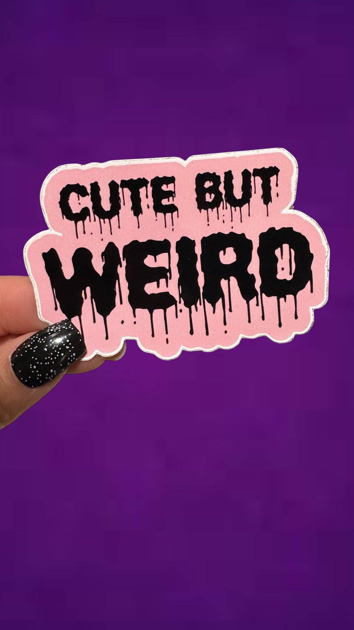 A hand with black glitter nail polish holds a die-cut sticker that reads &
