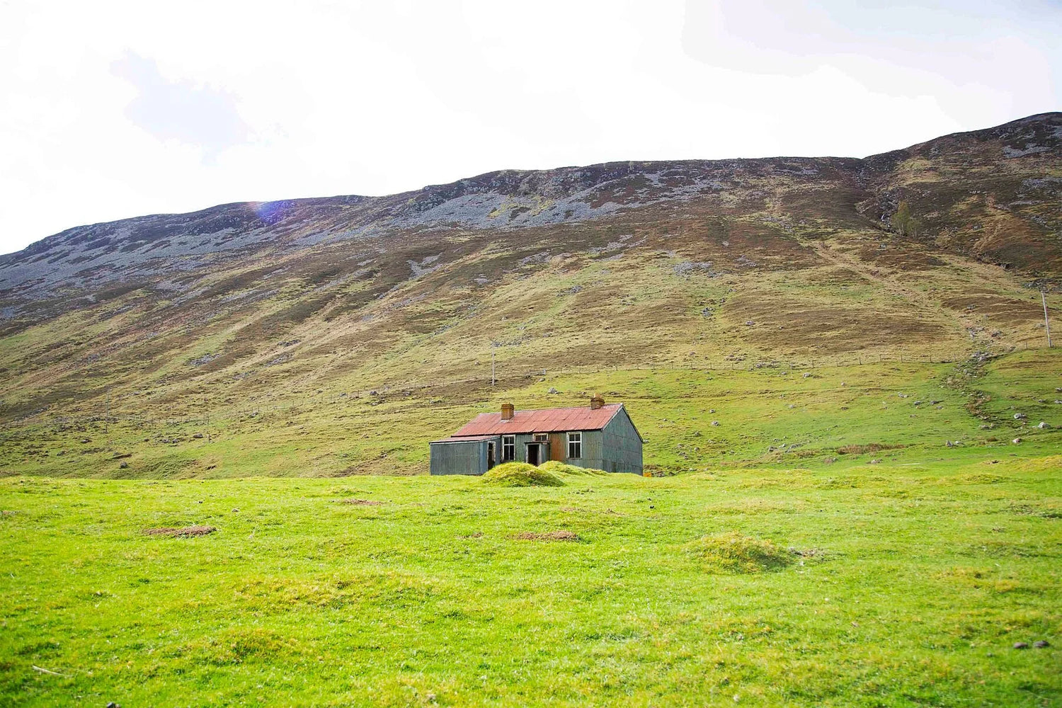 Photograph of an abandoned house in the green hills of a glen in Scotland.
