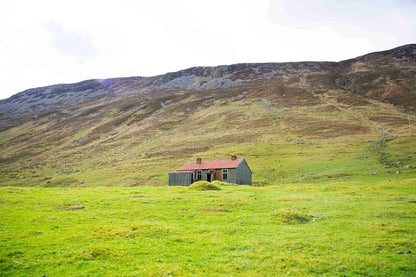 Photograph of an abandoned house in the green hills of a glen in Scotland.