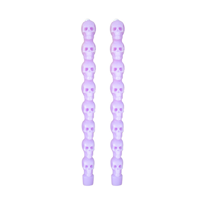 Pair of light purple taper candles molded as stacked skulls, on white.