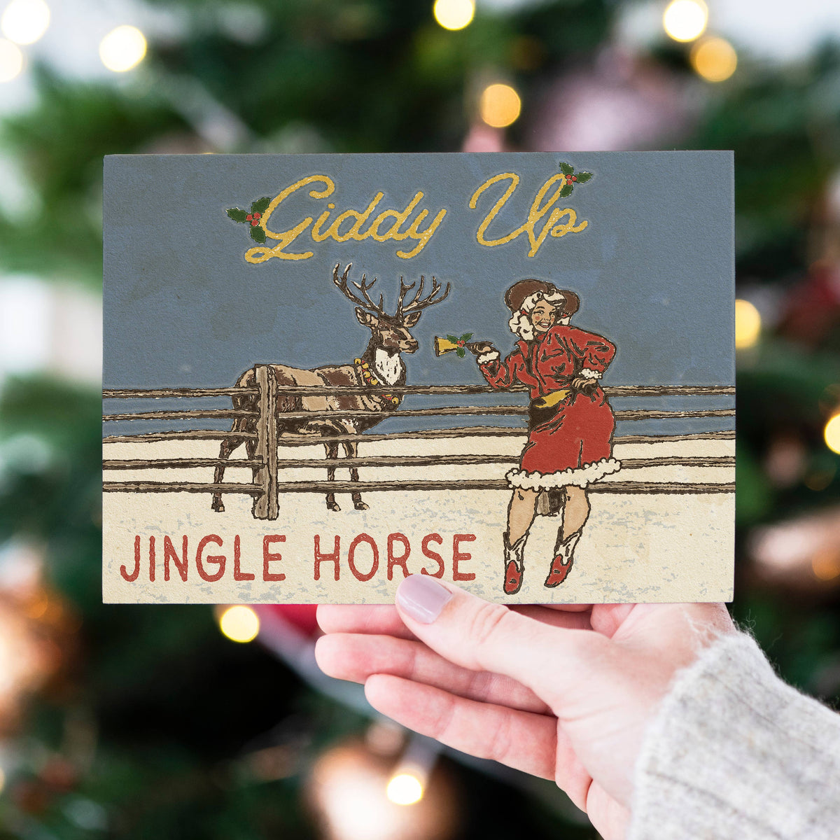 A hand holds a vintage-style Christmas card featuring the text &