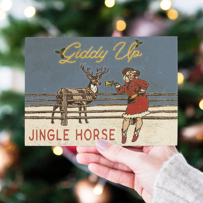 A hand holds a vintage-style Christmas card featuring the text &