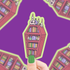 Hand holding a sticker of a bookshelf with books and candles against a purple background