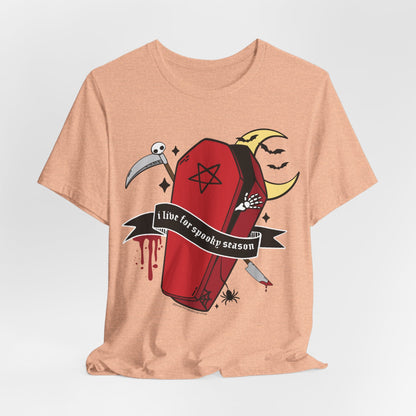 A peach-colored heather t-shirt with a gothic graphic of a red coffin, a scythe, a crescent moon face, and a banner that reads &