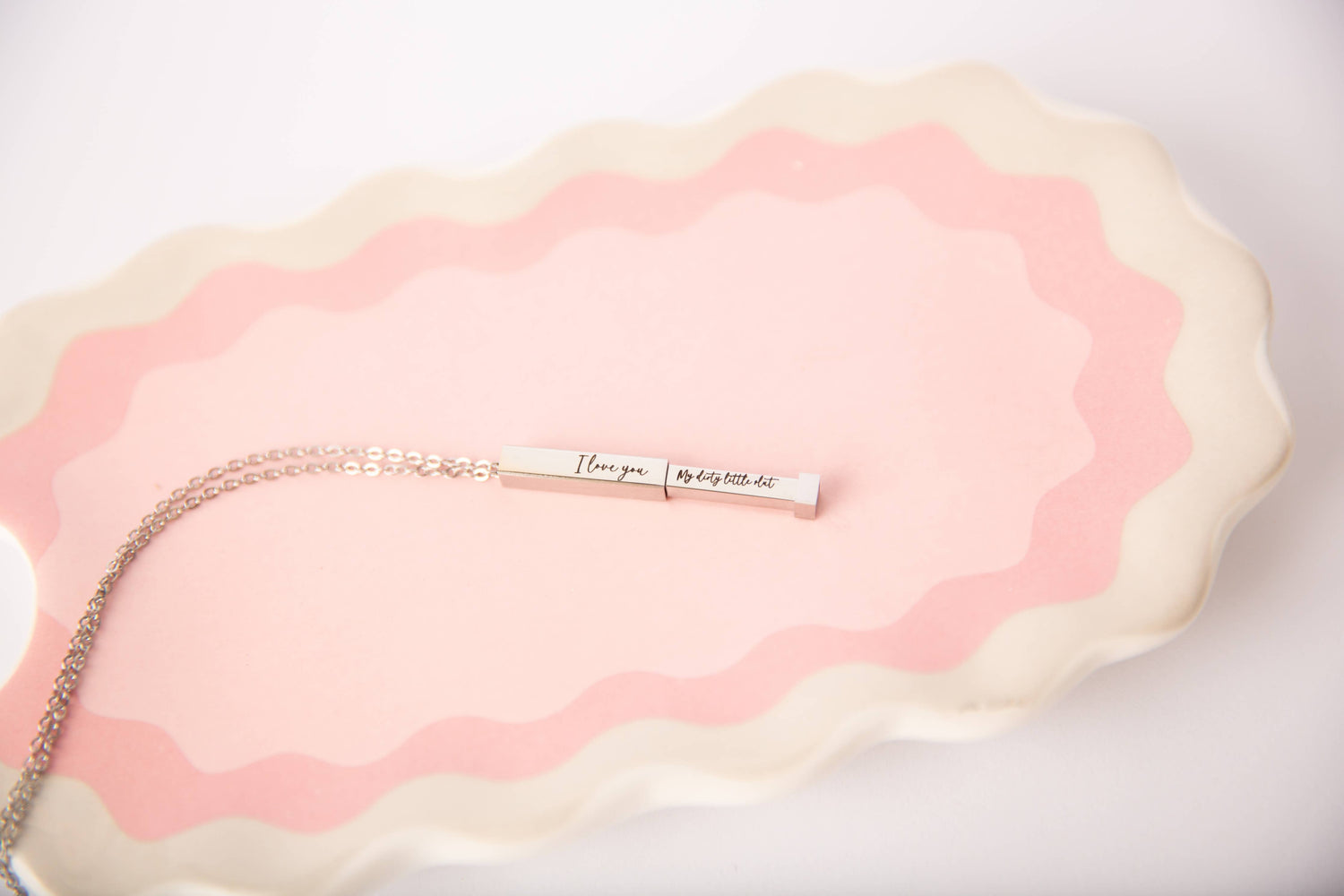 Necklace with a bar pendant on a pink and white textured surface