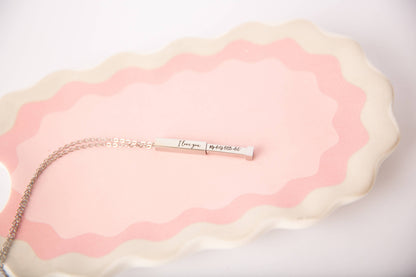Necklace with a bar pendant on a pink and white textured surface