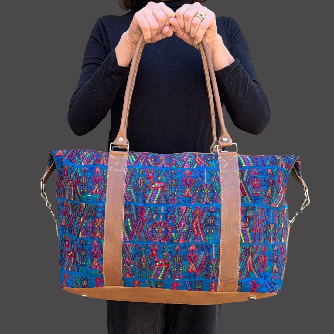 Person holding a colorful patterned bag with brown straps against a gray background