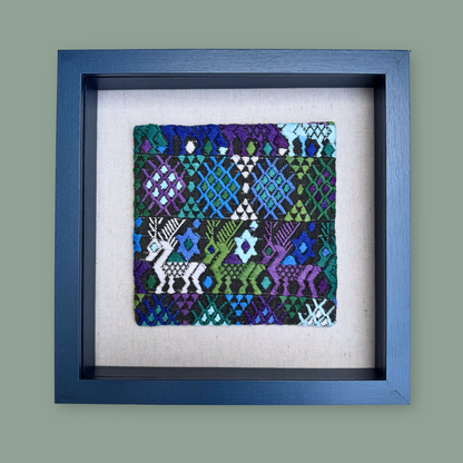 Framed textile art piece with geometric patterns and deer designs on a gray background