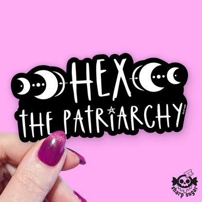 A hand with glittery purple fingernails holds a black die-cut sticker featuring white text reading &