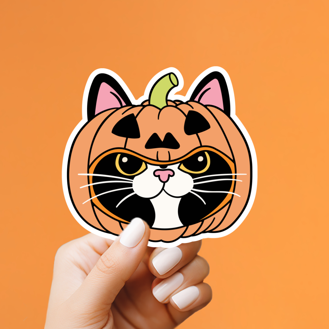 A hand with white manicured nails holds a die-cut sticker shaped like a pumpkin cat head. The sticker features an orange pumpkin body with black jack-o&