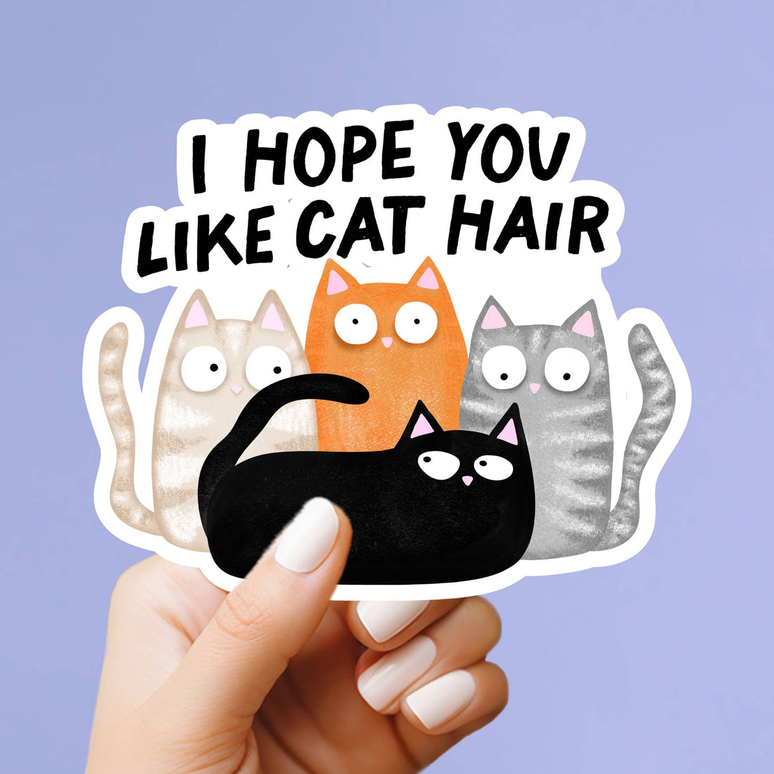 A hand with white manicured nails holds a die-cut sticker that reads &
