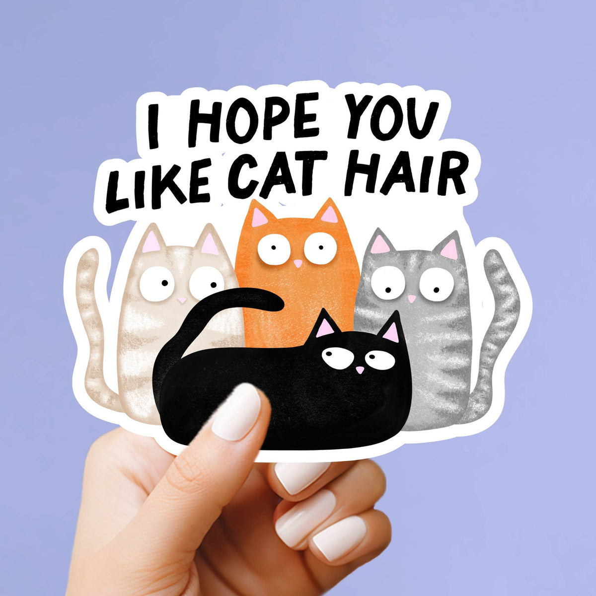 A hand with white manicured nails holds a die-cut sticker that reads &