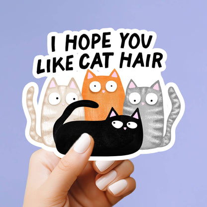 A hand with white manicured nails holds a die-cut sticker that reads &
