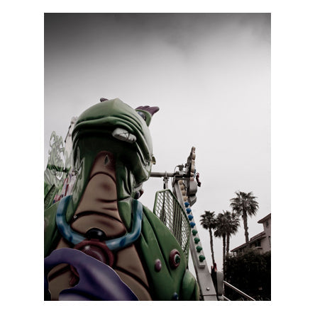 Image of a street carnival ride, featuring a green dragon with a broken tooth in front of the lights on the ride.