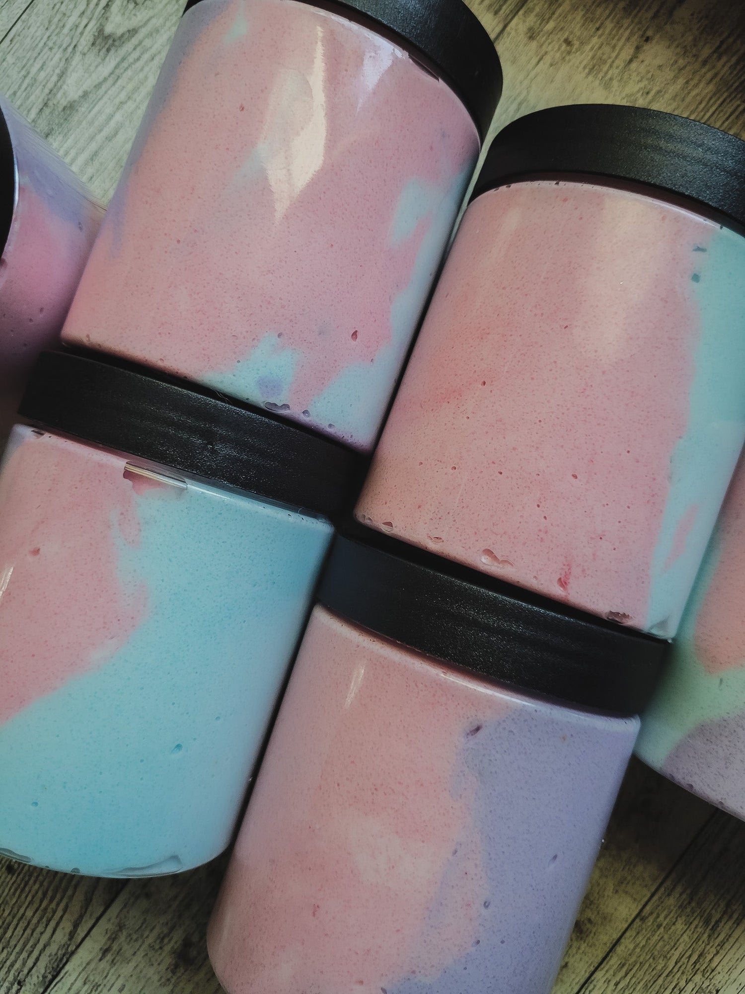 Two cylindrical containers with pink and blue speckled pattern and black lids on a wooden surface.