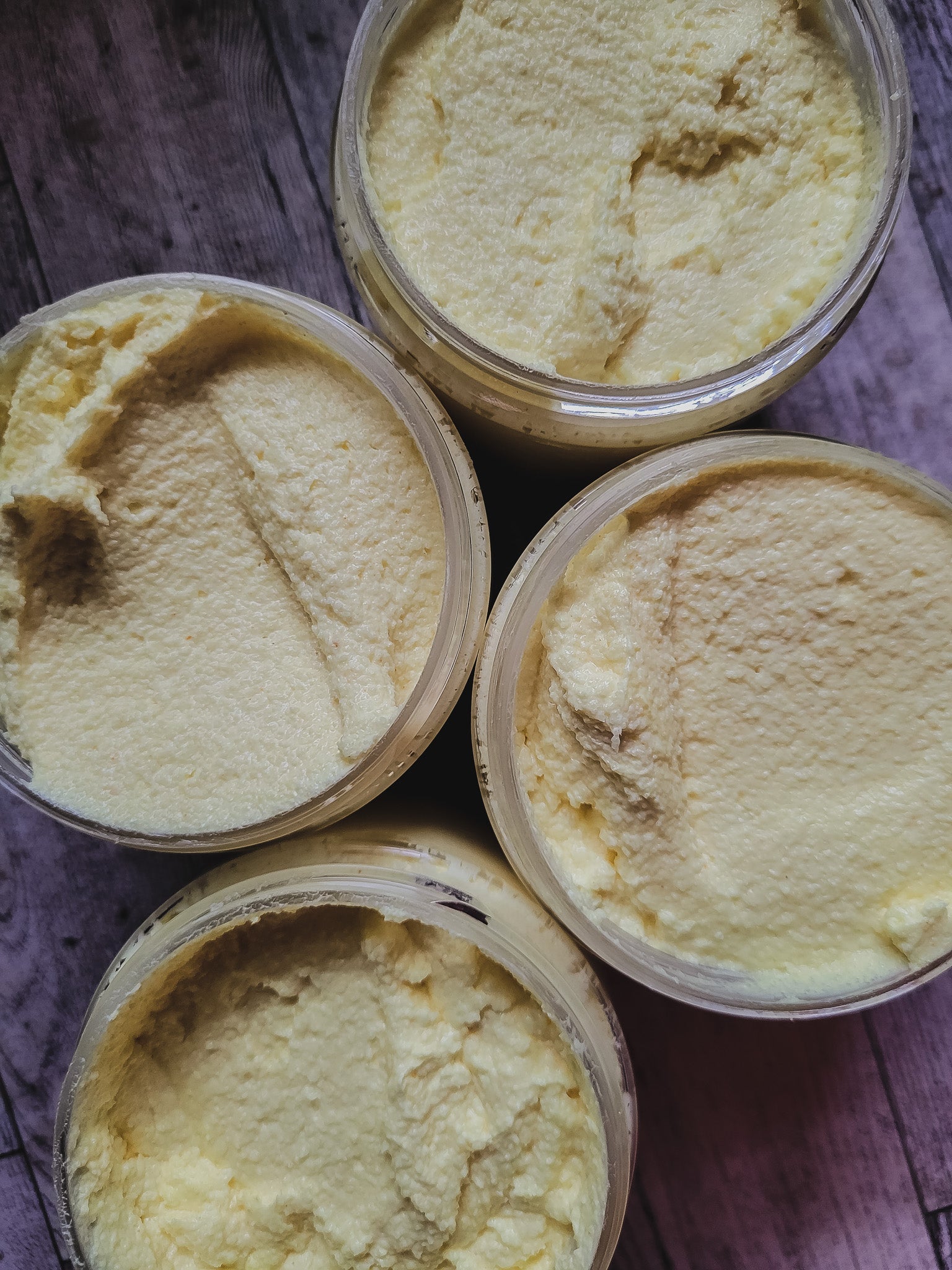 Four containers of yellow scrub on a wooden surface