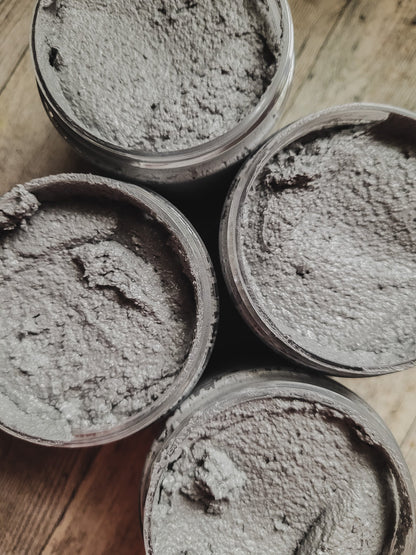 Four containers of grayish-brown scrub on a wooden surface