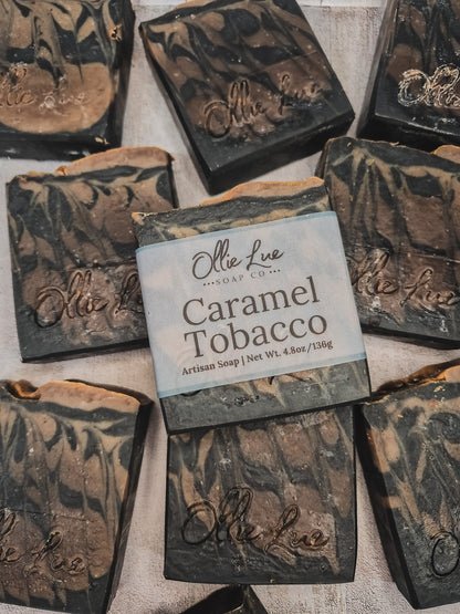 Several handmade soap bars are arranged on a light fabric background. The center soap is labeled &