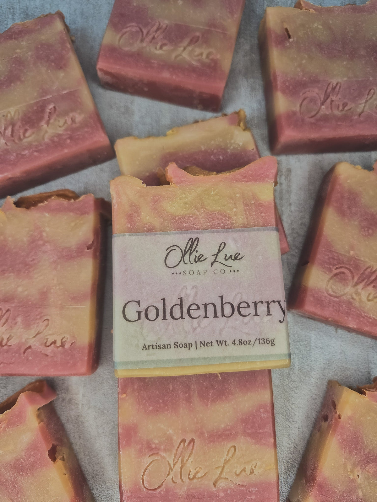 Artisan soap bars in a pink and golden-yellow marbled pattern, with a central bar wrapped in a paper label that reads &