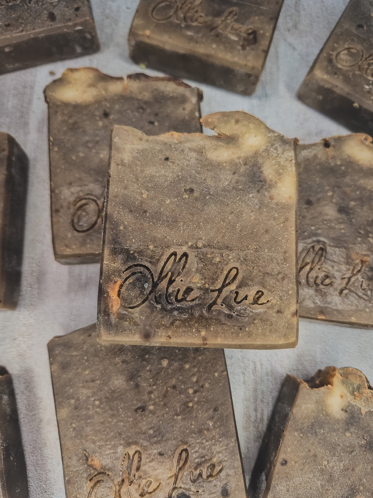 Several handmade rectangular bars of soap in a dark brown and beige marbled pattern, with the brand name &