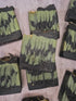Several handmade soap bars with a green and black marbled pattern are arranged on a textured light gray surface. The center soap bar is upright and features the brand name &