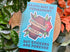 Notebook with a sticker on it, surrounded by plants