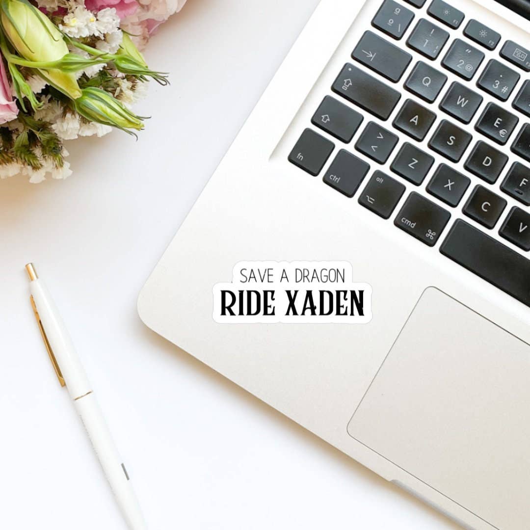 Laptop on a white surface with flowers and a pen, featuring text &