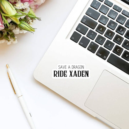 Laptop on a white surface with flowers and a pen, featuring text &