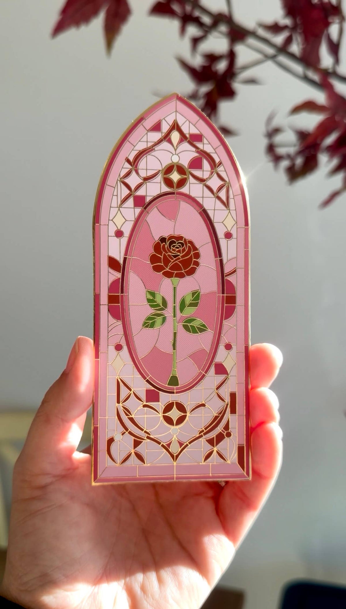 Decorative pink stained glass bookmark with floral design held by a hand against a blurred background