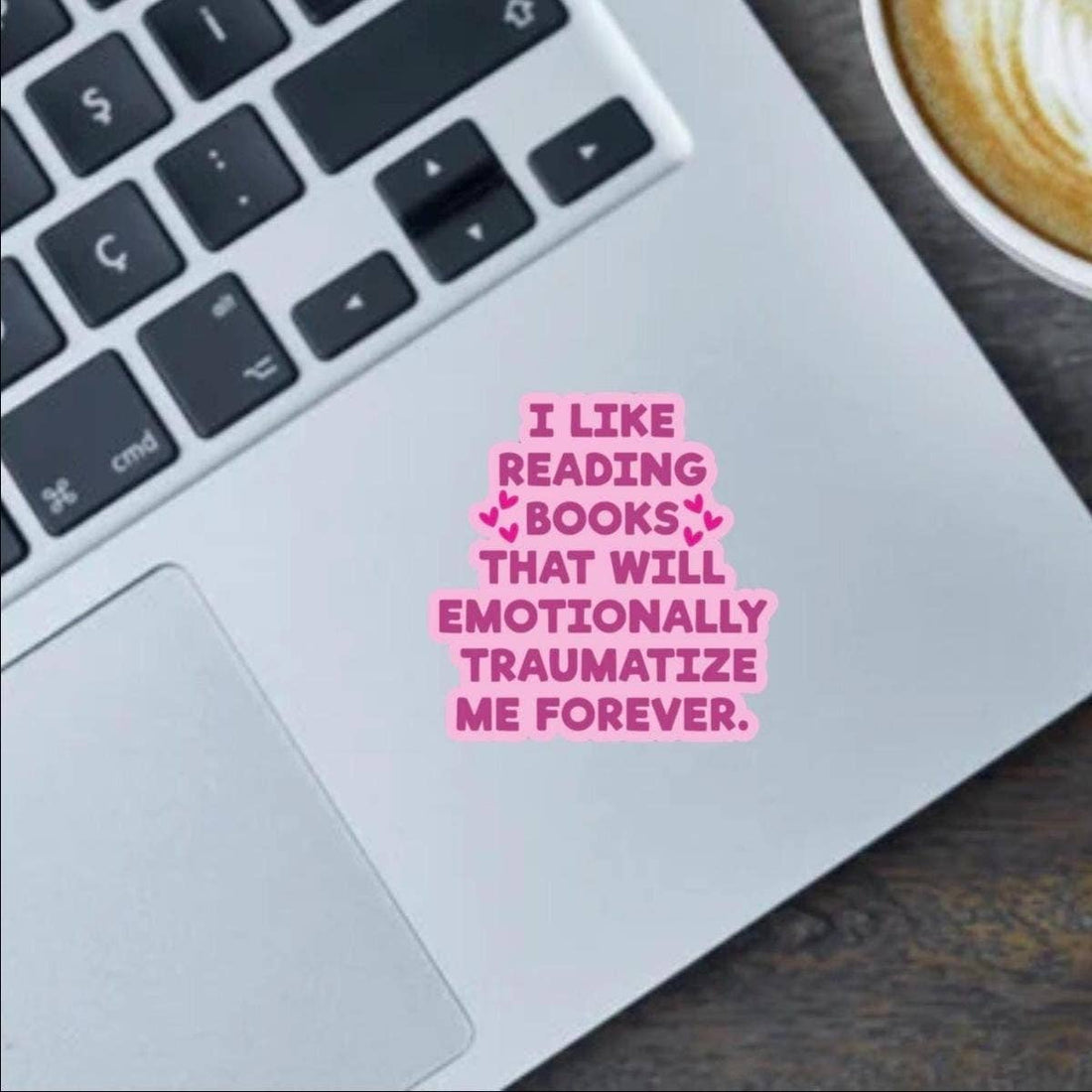 Laptop with a pink text sticker on the keyboard, next to a cup of coffee.