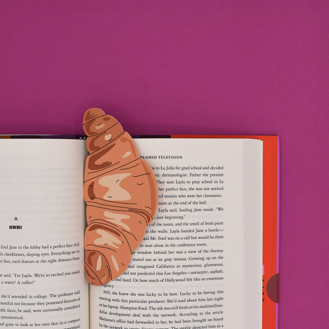 Croissant-shaped bookmark on an open book with a pink background