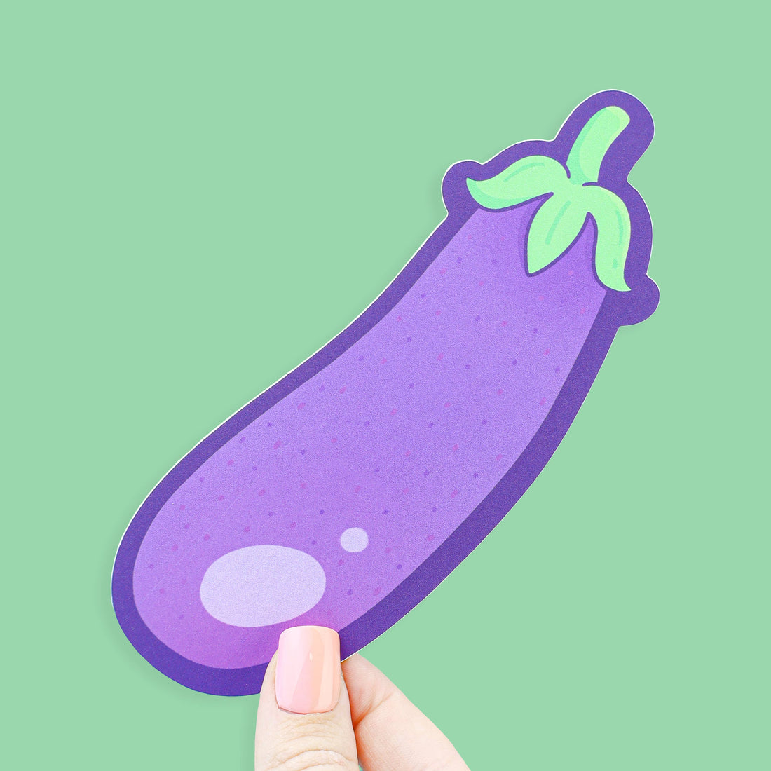Hand holding a purple eggplant-shaped sticker against a green background