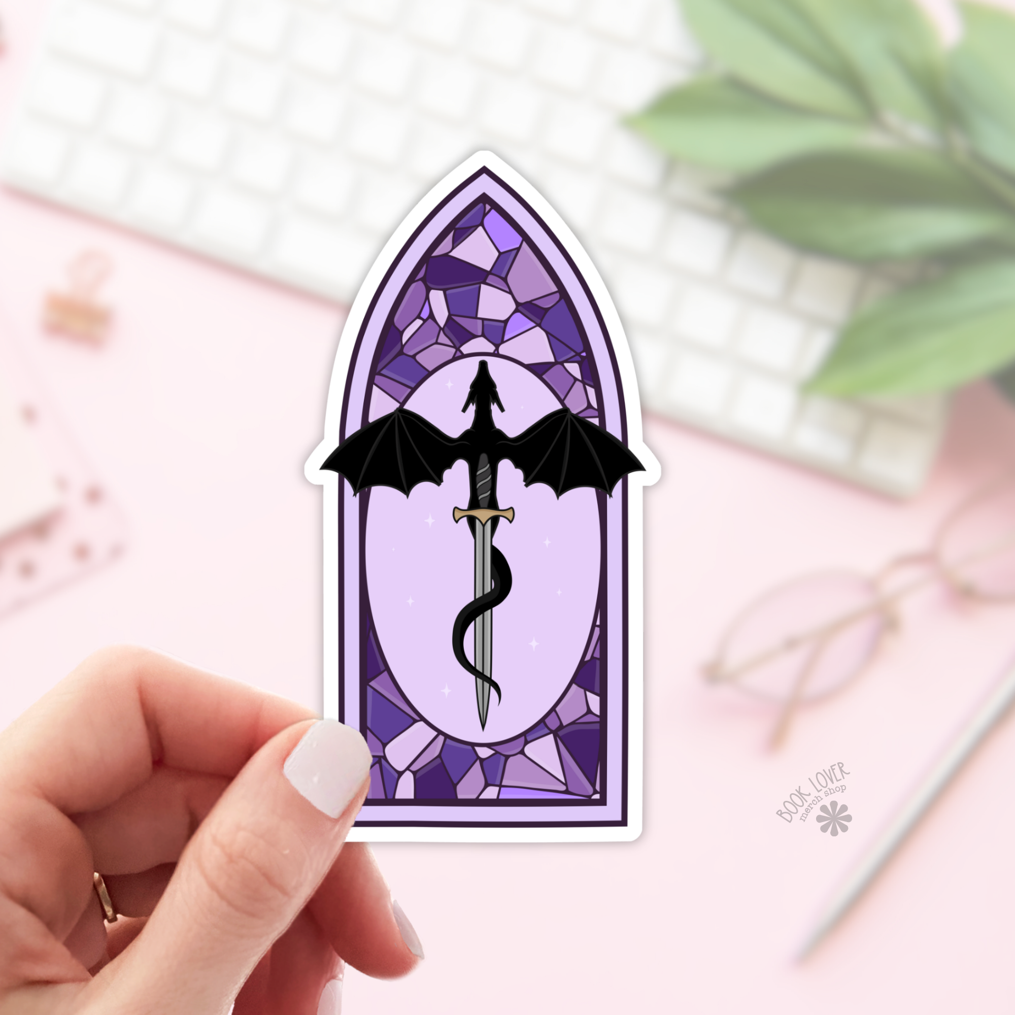 Sticker of a dragon and sword design in a stained glass window style held by a hand.