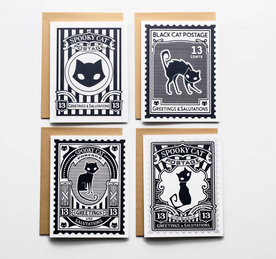 Four Halloween-themed postage stamp greeting cards arranged in a 2x2 grid on a white background, each with a kraft envelope behind it. The stamps feature black cats, vintage typography, and designs in black, white, and navy tones.