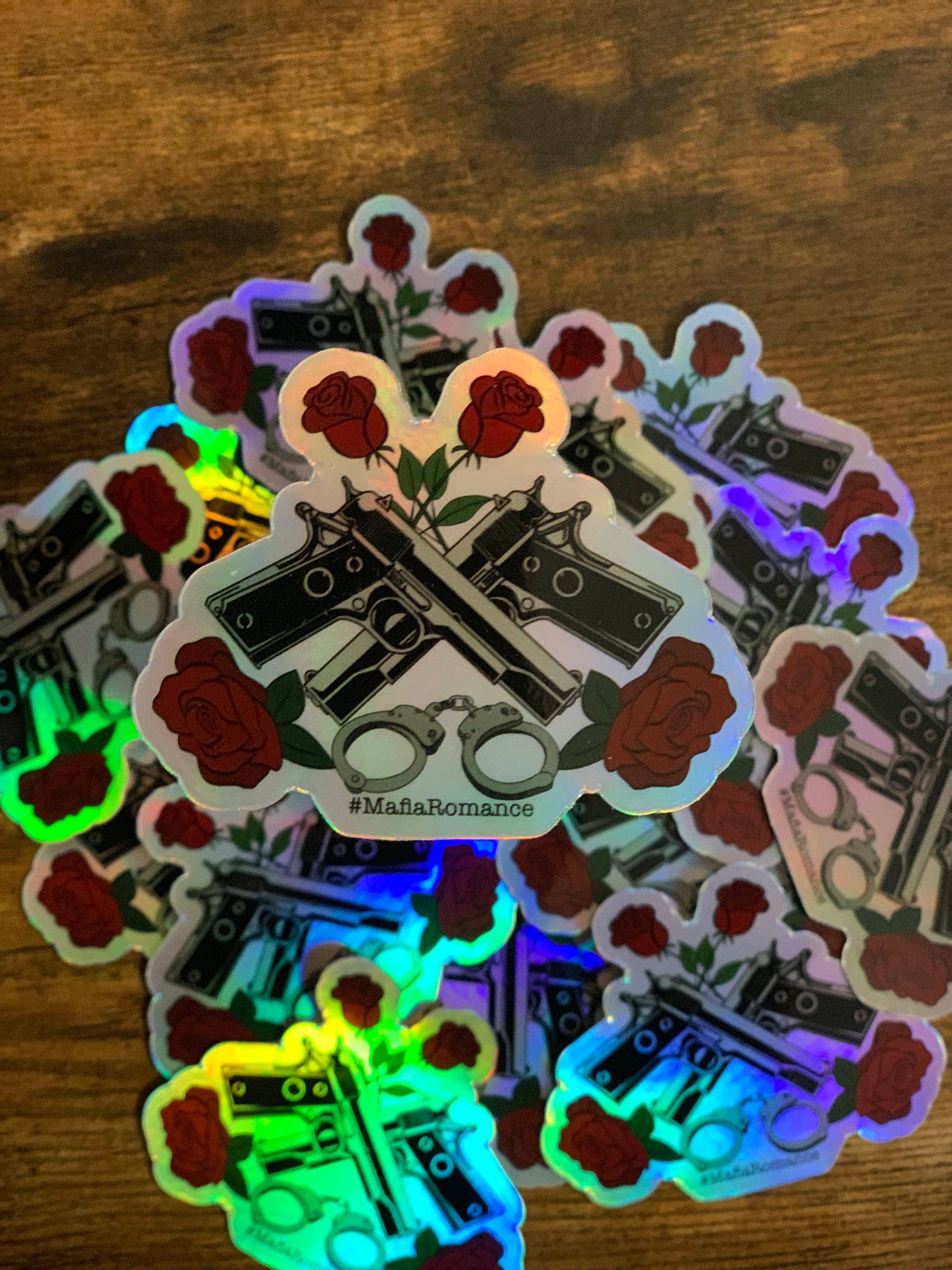 Holographic stickers with roses, guns, and handcuffs on a wooden surface