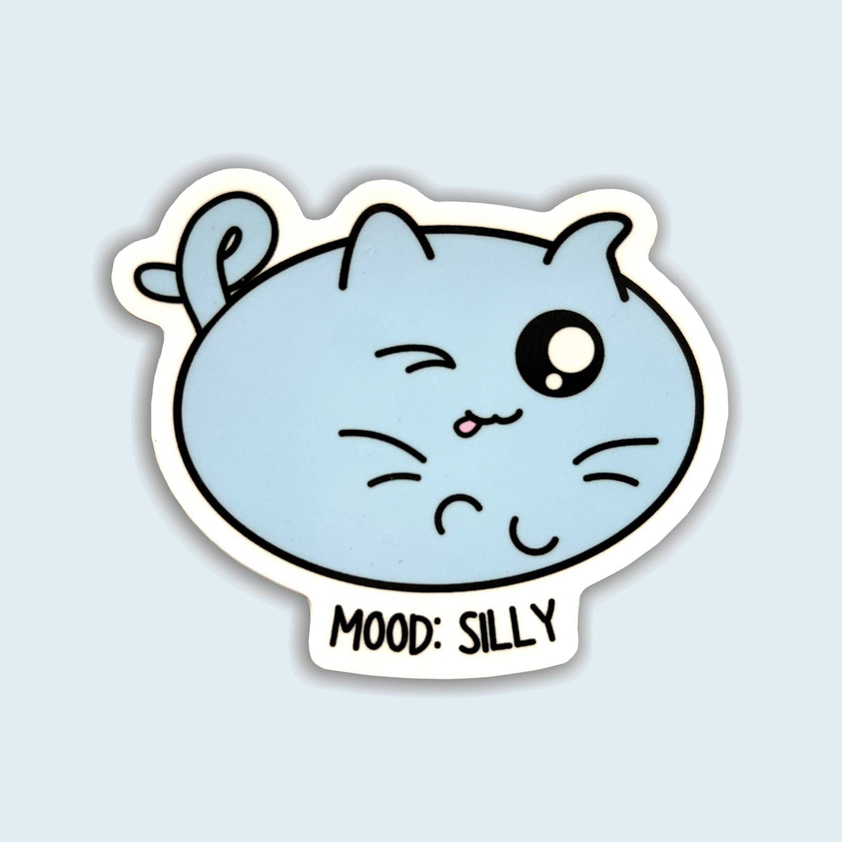 A die-cut sticker featuring a light blue cartoon cat face with one winking eye and the text &