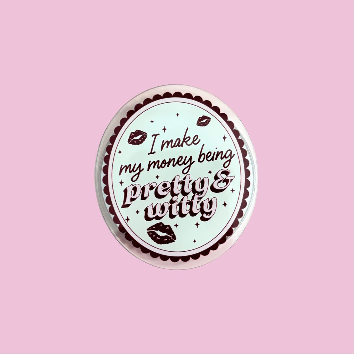 A circular button with the text "I make my money being pretty &amp; witty" printed on it, set against a pink background.