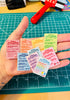 Hand holding small reminder notes with colorful text on a green cutting mat.