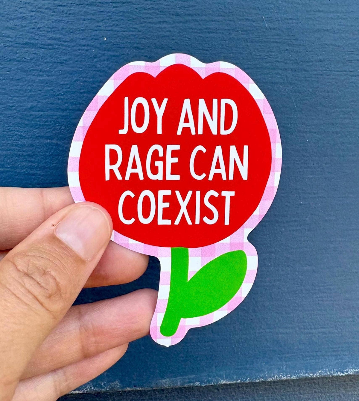 Hand holding a red flower-shaped sticker with &