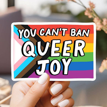 Hand holding a rainbow-colored sticker with text &