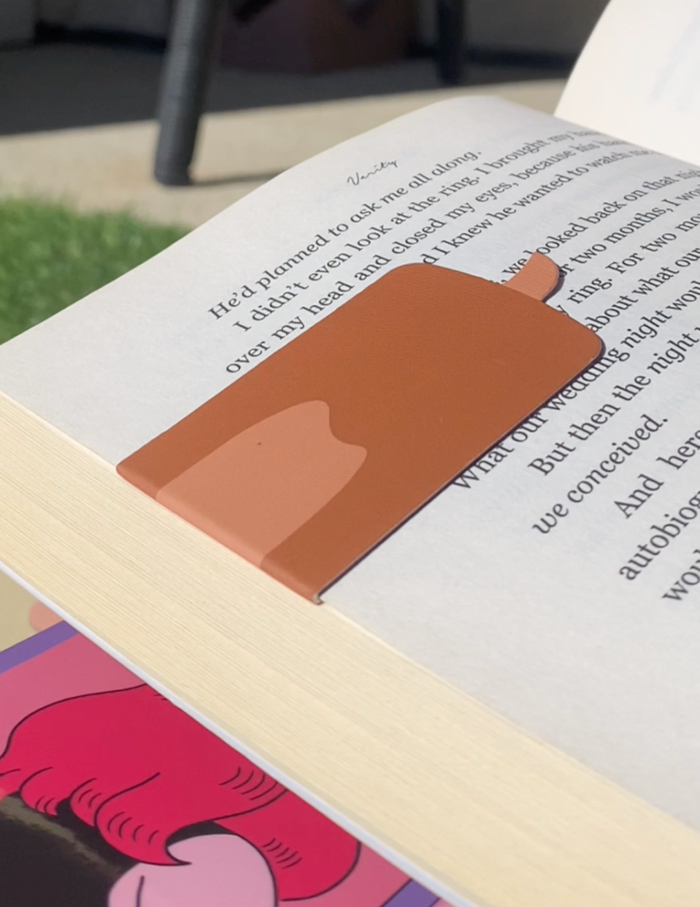 Open book with a bookmark featuring a brown object on a grassy outdoor background