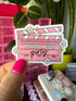 A hand with bright pink nail polish holds a die-cut sticker shaped like a pink horror movie clapperboard. The sticker has white daisy flowers, yellow stars, and the text &