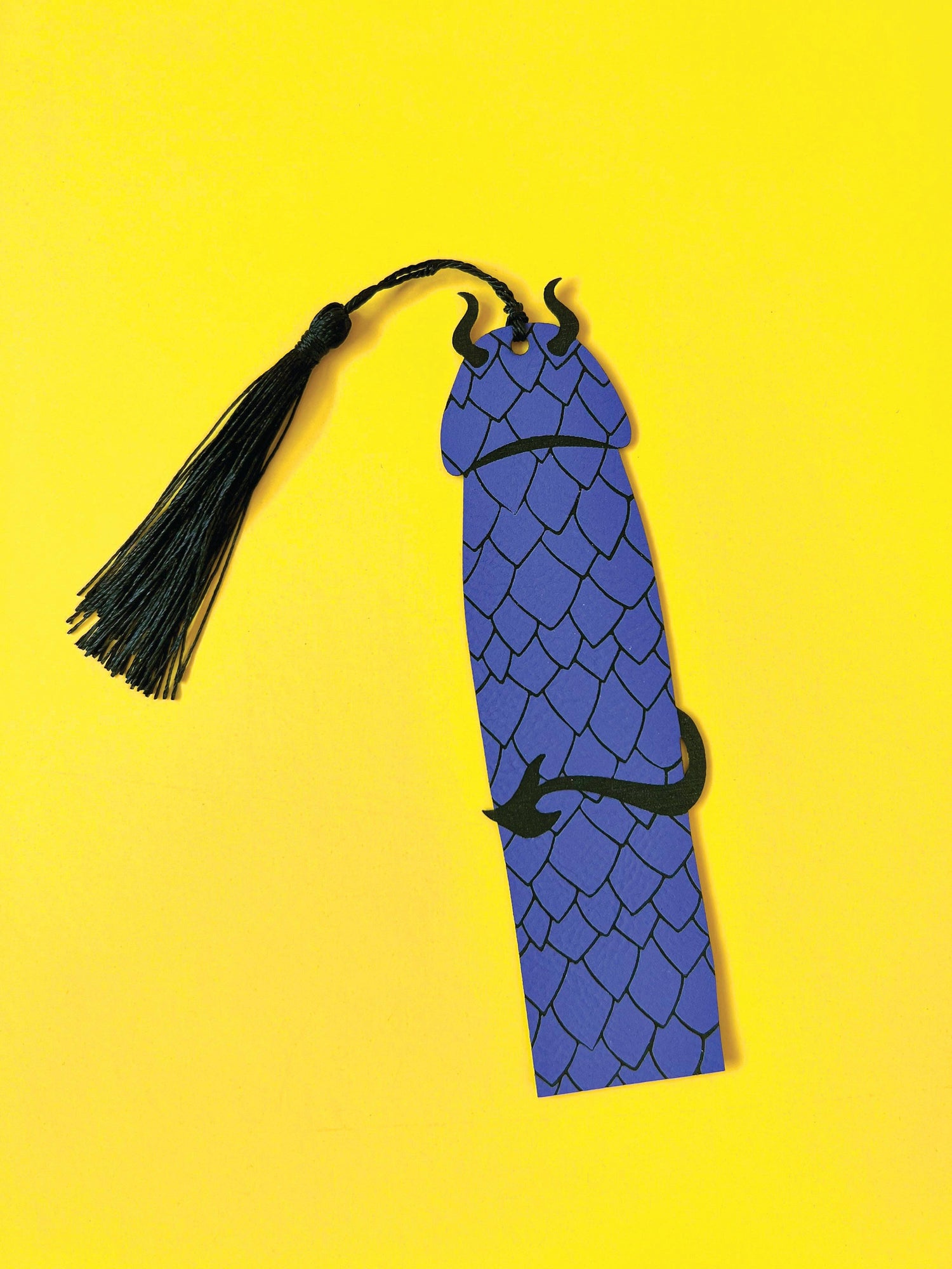 Blue dragon-shaped bookmark with a black tassel on a yellow background