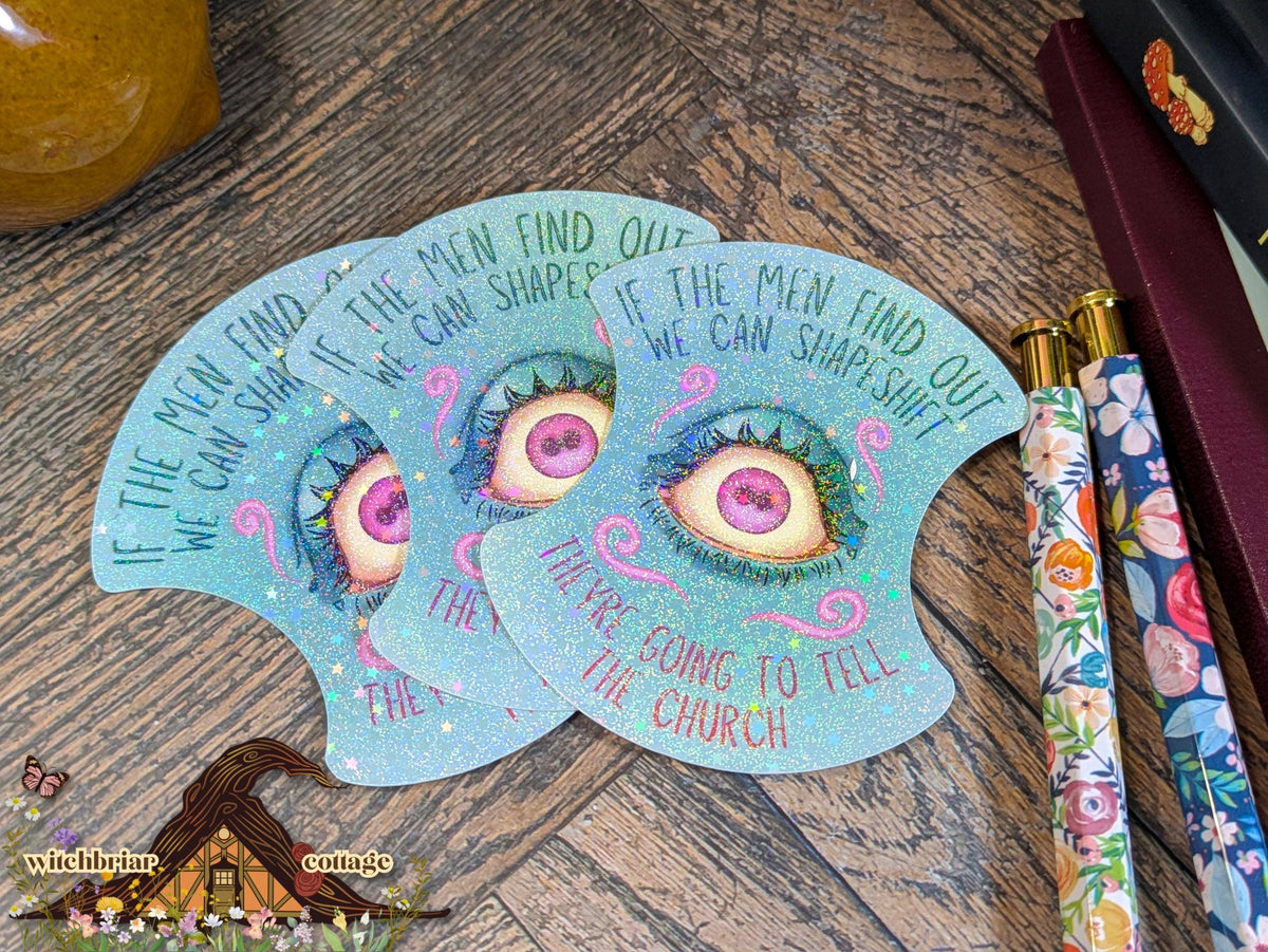 Three blue eye-shaped stickers with text on a wooden surface with a pen and decorative items.