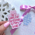 A hand with pink nail polish holds a scalloped gift box-shaped sticker that reads &